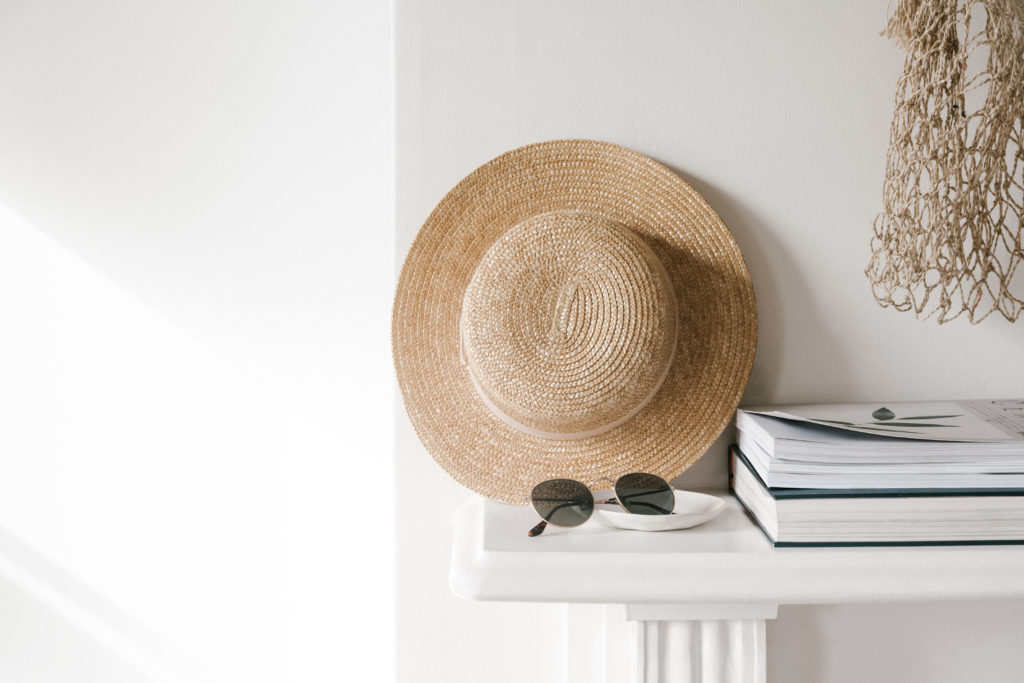 a mantle in a home with a straw hat, sunglasses, and books neatly arranged on top of it