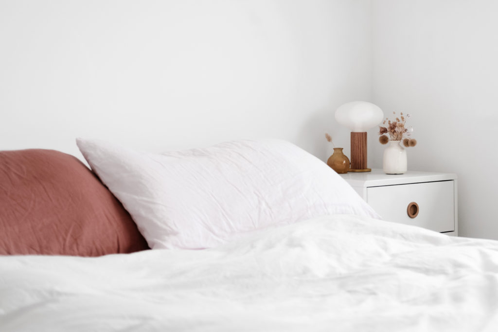 a healthy home depicted as a minimalist bedroom with white walls, white wooden side table, and linen bedding